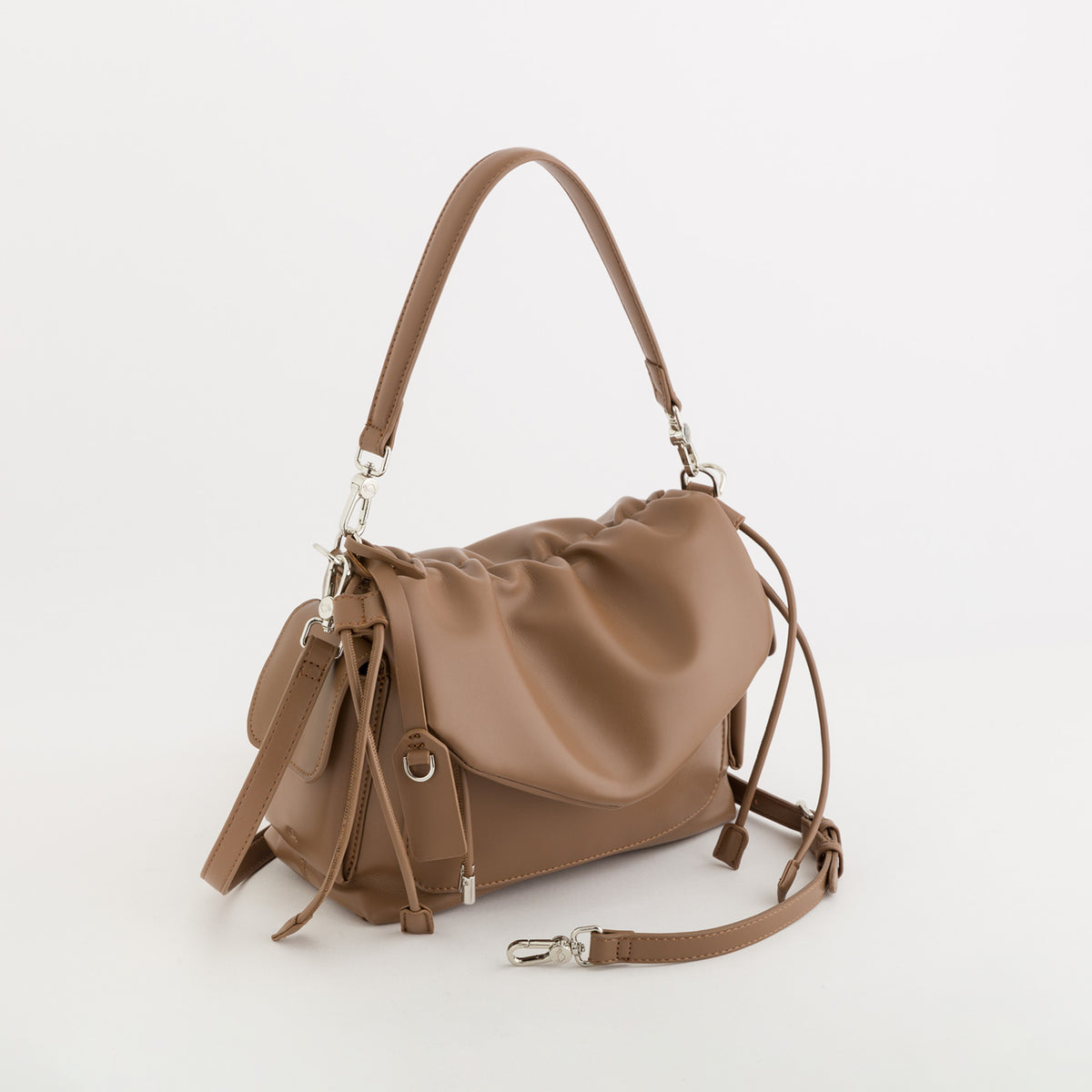 A taupe brown leather shoulder bag with a slouchy, gathered silhouette, featuring a top handle, a front flap pocket with a drawstring detail, and an adjustable shoulder strap with silver-tone hardware, set against a plain white background.